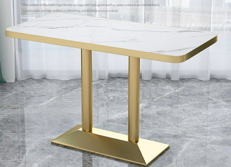 Table rectangulaire au design moderne présente un plateau à effet marbre blanc et des pieds doubles en métal doré.
