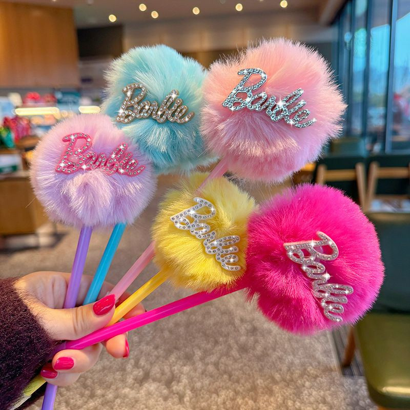 Stylos à pompon en peluche Barbie se distinguent par leurs boules duveteuses aux couleurs pastel et éclatantes, surmontées de l'inscription « Barbie » en strass scintillants.